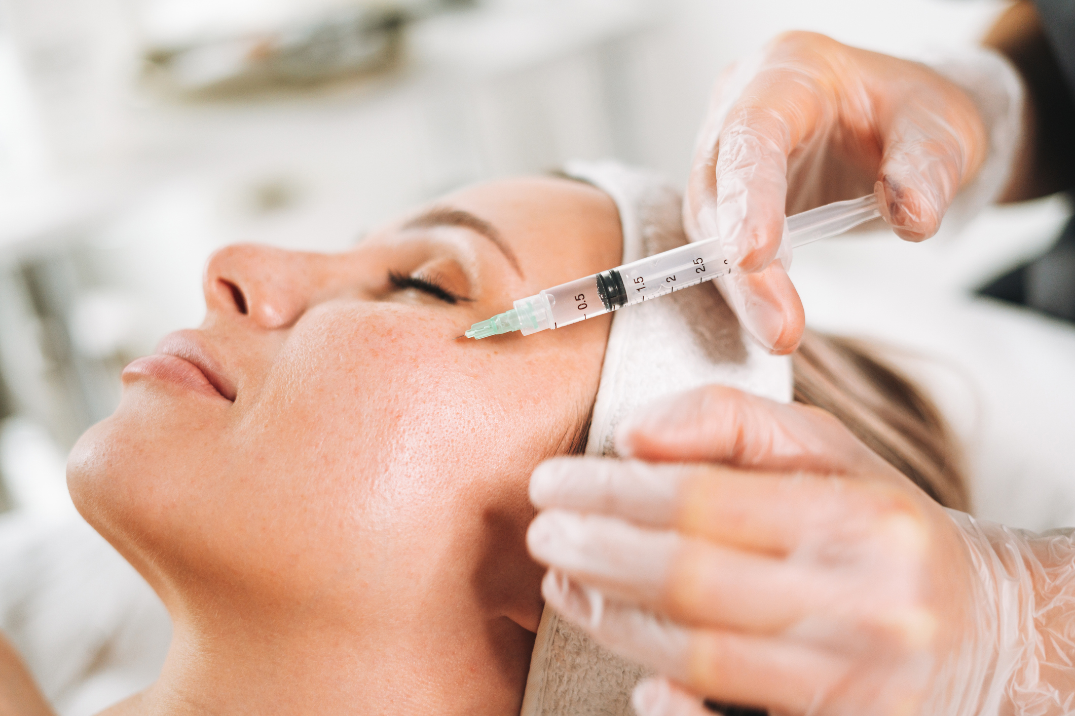 Young woman getting cosmetic injections in her face while lying on couch in beauty salon Botox